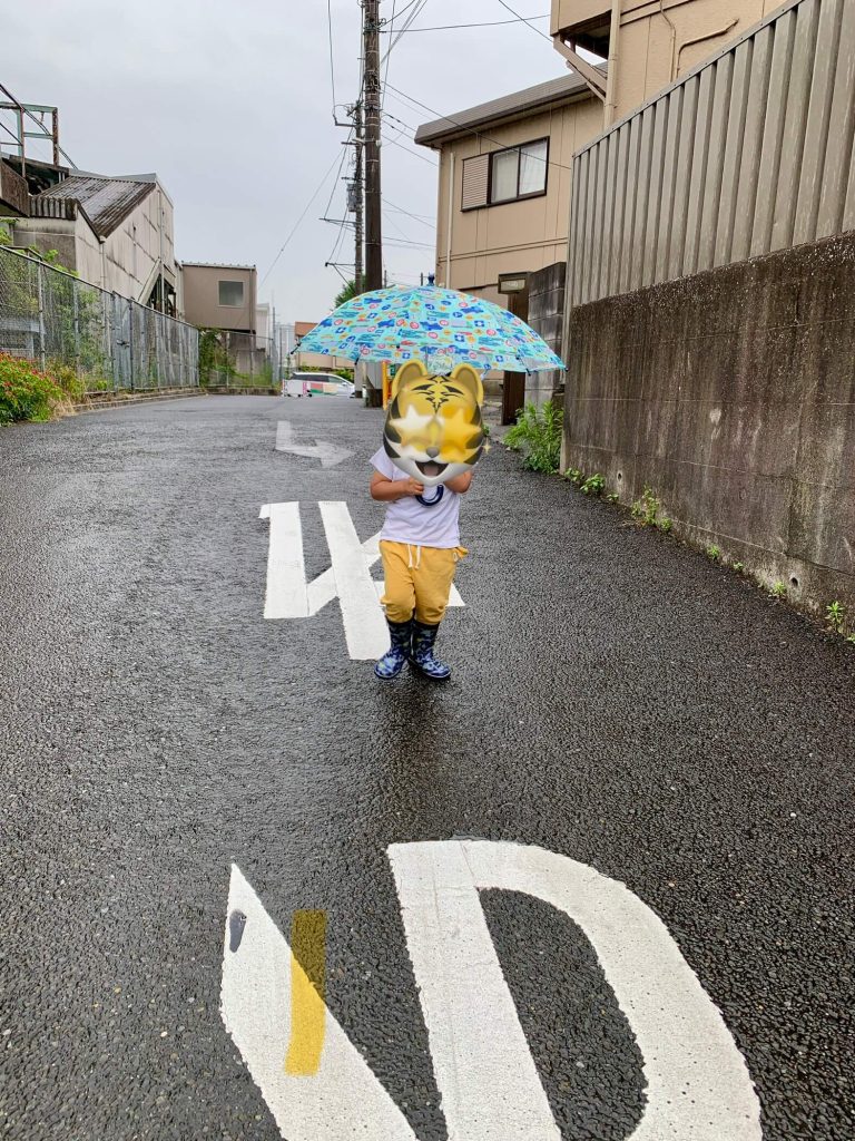 My son with umbrella and rain boots walking through light June rain
